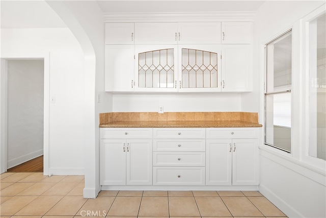 kitchen with baseboards, light stone countertops, light tile patterned floors, arched walkways, and white cabinets