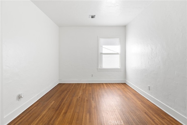 spare room with visible vents, baseboards, and wood-type flooring