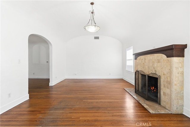 unfurnished living room featuring visible vents, a tile fireplace, wood finished floors, baseboards, and vaulted ceiling