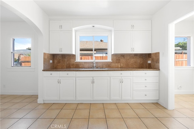 kitchen featuring light tile patterned floors, baseboards, a sink, white cabinetry, and tasteful backsplash