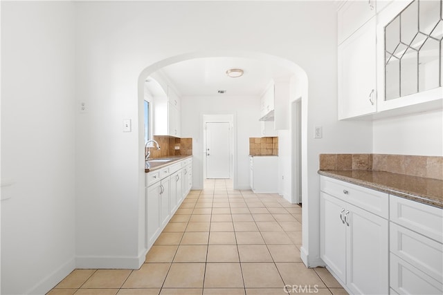 kitchen featuring decorative backsplash, white cabinets, light tile patterned flooring, and a sink