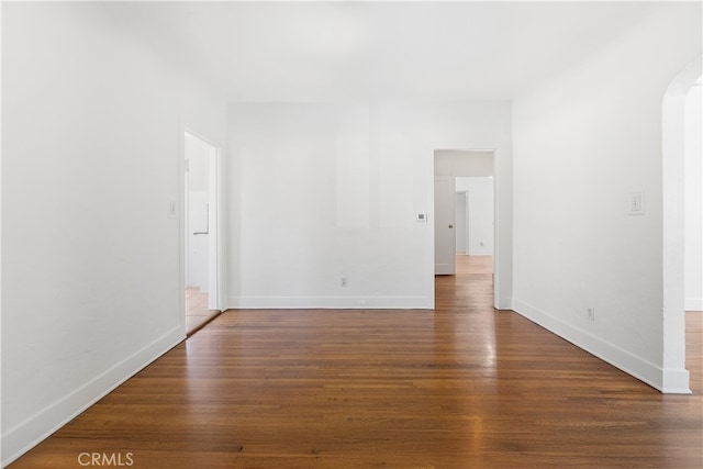 spare room featuring arched walkways, baseboards, and wood finished floors