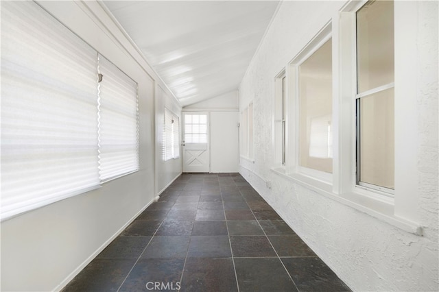 hallway with stone tile flooring, baseboards, and vaulted ceiling