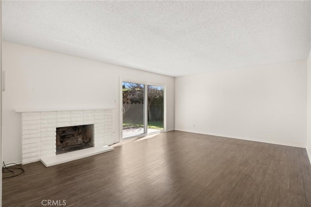 unfurnished living room with dark wood finished floors, baseboards, a textured ceiling, and a brick fireplace