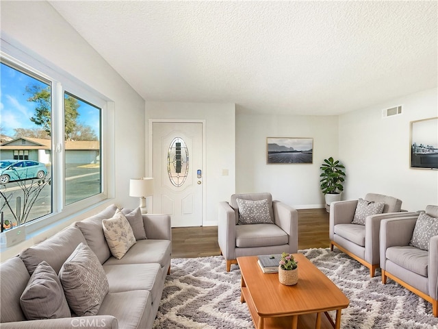 living area featuring a textured ceiling, wood finished floors, visible vents, and baseboards