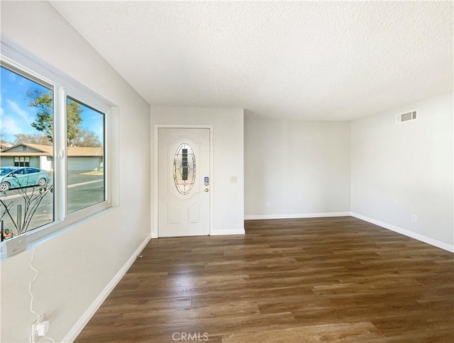 foyer entrance with a textured ceiling, dark wood-style flooring, visible vents, and baseboards