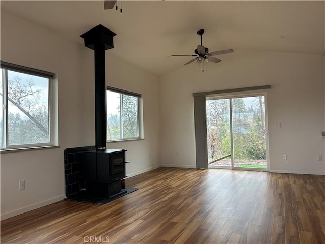 unfurnished living room featuring baseboards, a ceiling fan, wood finished floors, a wood stove, and vaulted ceiling