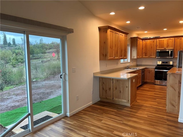 kitchen with stainless steel appliances, light countertops, light wood-type flooring, a sink, and recessed lighting