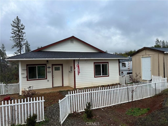 bungalow-style home featuring a fenced front yard, roof with shingles, an outdoor structure, and a storage shed