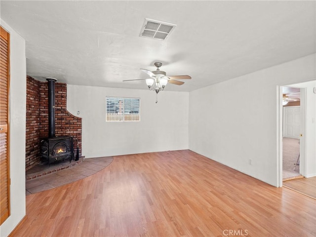 unfurnished living room with visible vents, light wood-style floors, a wood stove, and a ceiling fan