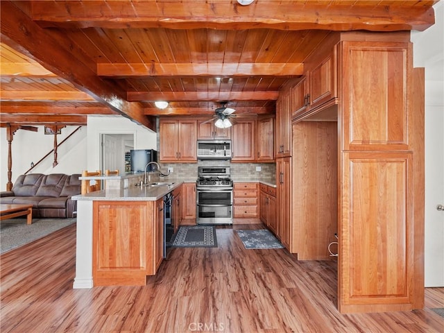 kitchen featuring brown cabinets, wood finished floors, open floor plan, stainless steel appliances, and a peninsula