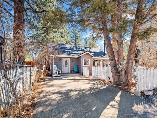 view of front facade featuring a gate, a fenced front yard, a shingled roof, and aphalt driveway