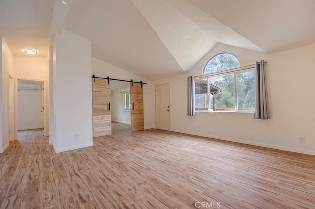 interior space featuring light wood-style flooring, baseboards, vaulted ceiling, and a barn door