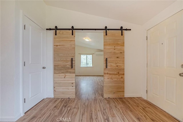 empty room with lofted ceiling, light wood finished floors, and a barn door