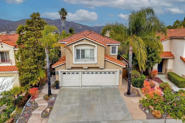 mediterranean / spanish-style home featuring a garage, driveway, a tiled roof, a mountain view, and stucco siding