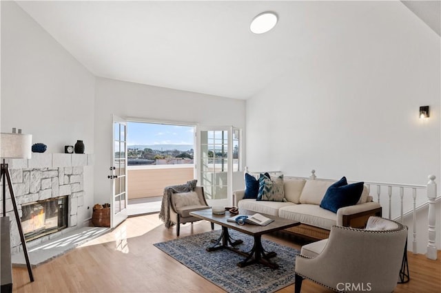 living room featuring lofted ceiling, a stone fireplace, and light wood-type flooring