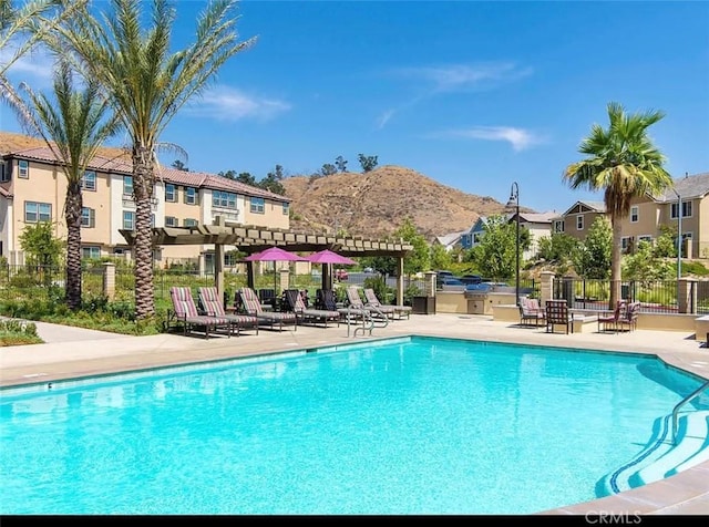 community pool with fence, a mountain view, and a patio