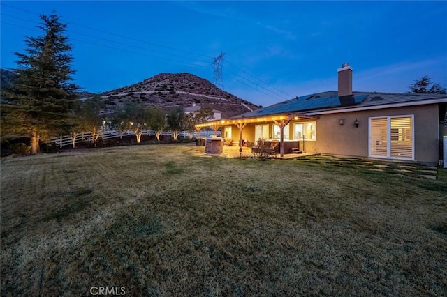 rear view of house featuring a lawn, stucco siding, a mountain view, and roof mounted solar panels