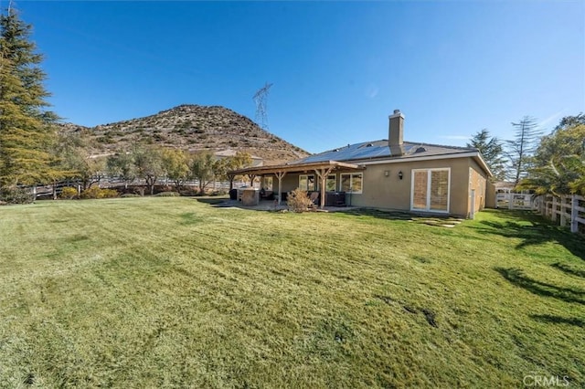 rear view of property featuring solar panels, a lawn, a chimney, fence, and a mountain view