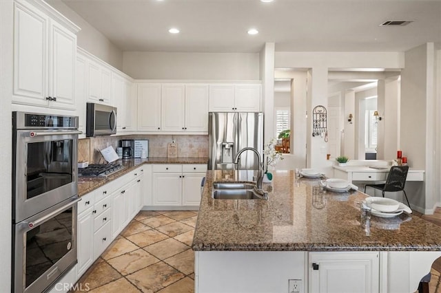 kitchen featuring a large island, stainless steel appliances, white cabinets, a sink, and dark stone counters