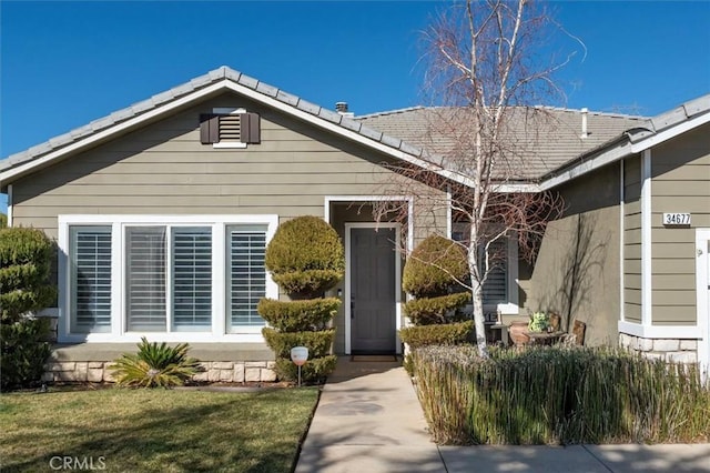 view of front of property featuring stone siding, a front lawn, and a tiled roof