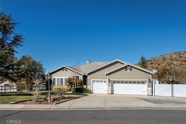 view of front of house with a garage, concrete driveway, stone siding, fence, and a mountain view