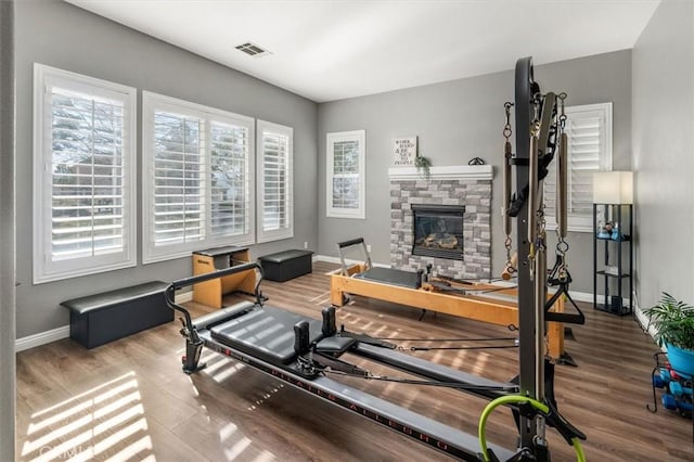 workout area with visible vents, a fireplace, baseboards, and wood finished floors