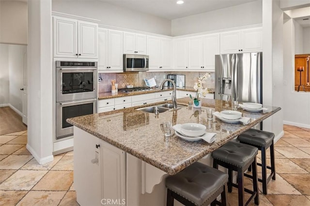 kitchen featuring stainless steel appliances, white cabinetry, and an island with sink