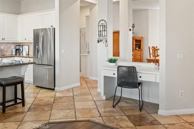 kitchen with built in study area, stainless steel refrigerator with ice dispenser, a breakfast bar area, and white cabinetry