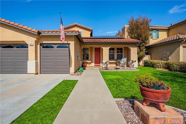 mediterranean / spanish-style house featuring stucco siding, solar panels, concrete driveway, an attached garage, and a front yard