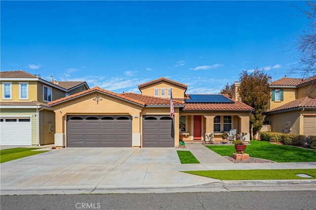 mediterranean / spanish-style home featuring stucco siding, covered porch, a front yard, roof mounted solar panels, and a garage