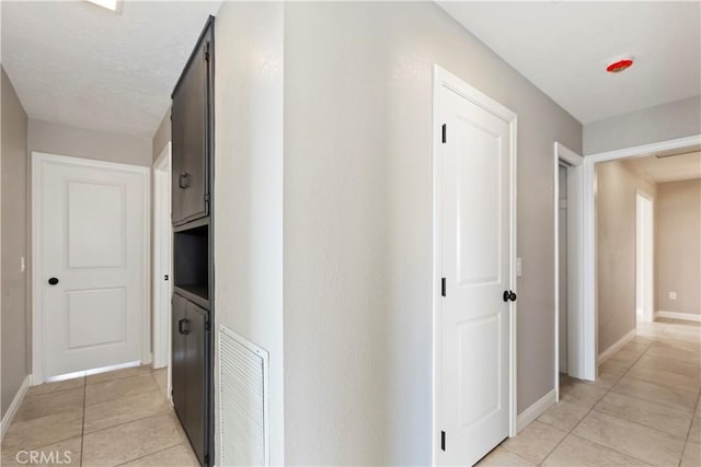 corridor with visible vents, baseboards, and light tile patterned floors