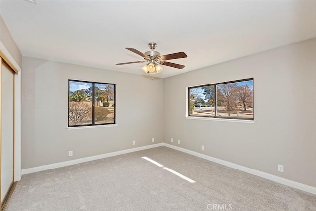 empty room with plenty of natural light, baseboards, a ceiling fan, and light colored carpet