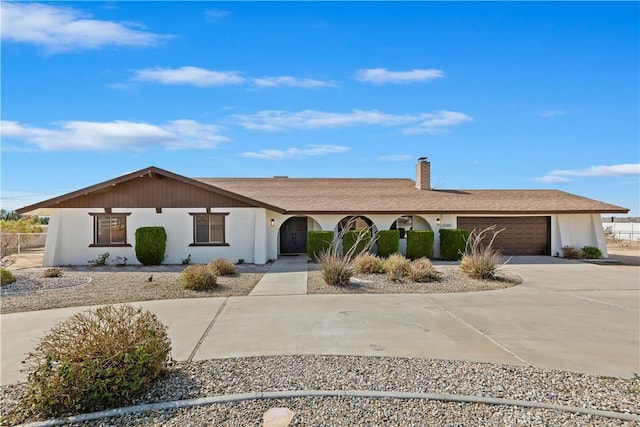 ranch-style house featuring concrete driveway, a chimney, an attached garage, and stucco siding