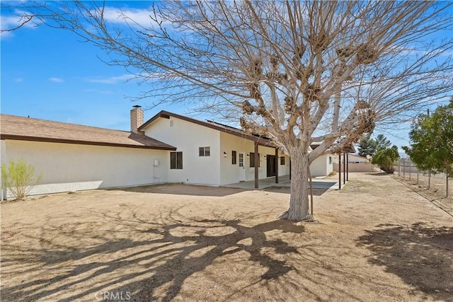 back of property featuring a patio area, a chimney, fence, and stucco siding