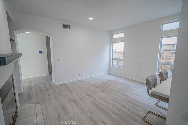 interior space featuring arched walkways, light wood-style flooring, visible vents, baseboards, and a tiled fireplace