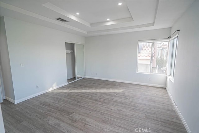 unfurnished bedroom featuring baseboards, visible vents, a raised ceiling, wood finished floors, and recessed lighting