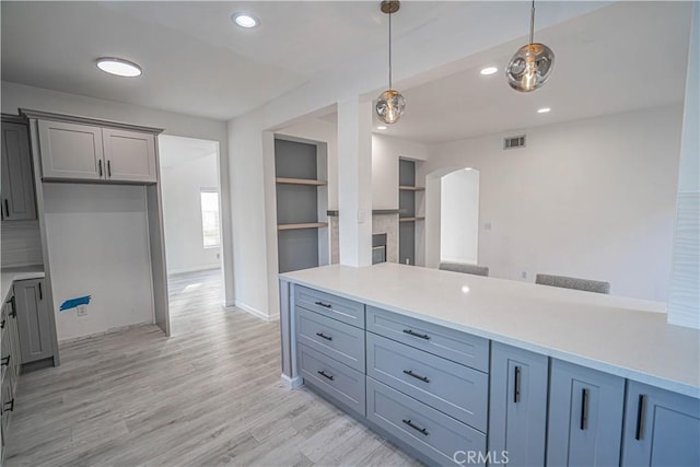 kitchen featuring arched walkways, light wood-style flooring, visible vents, light countertops, and decorative light fixtures