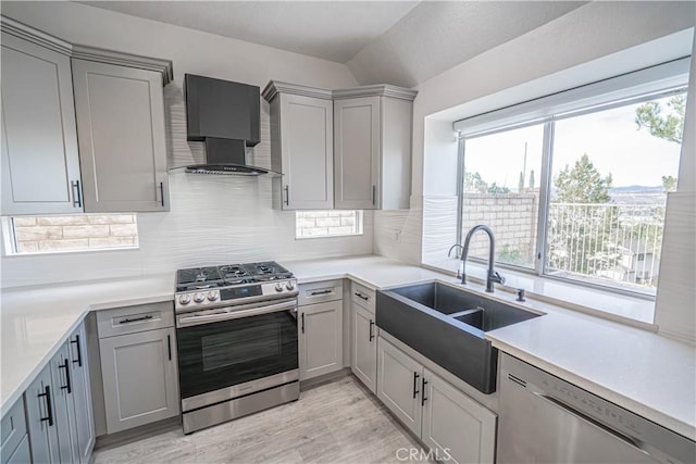 kitchen featuring gray cabinets, light countertops, appliances with stainless steel finishes, a sink, and wall chimney range hood