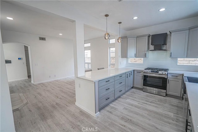 kitchen featuring stainless steel gas range oven, visible vents, arched walkways, a peninsula, and light countertops