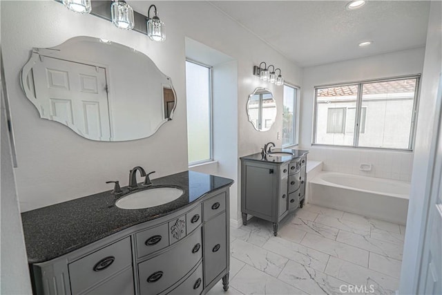 full bathroom with a bath, marble finish floor, two vanities, and a sink