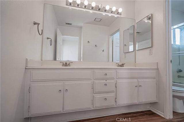 full bathroom with bath / shower combo with glass door, double vanity, visible vents, toilet, and wood finished floors