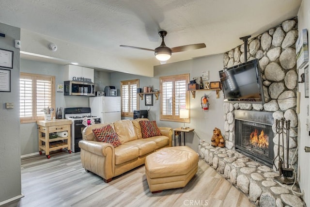 living area with light wood finished floors, a fireplace, a wealth of natural light, and a ceiling fan