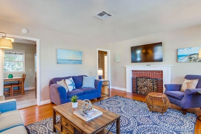 living area featuring a brick fireplace, wood finished floors, visible vents, and baseboards