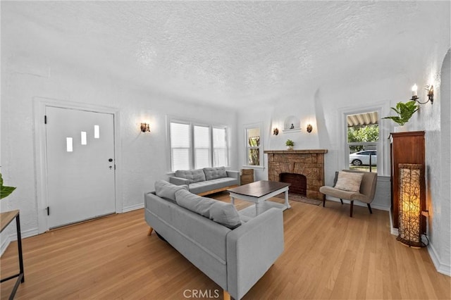 living room with a textured ceiling, a fireplace, light wood-style flooring, and baseboards