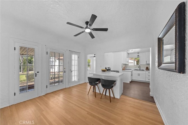 kitchen with a sink, light wood-style floors, white cabinets, light countertops, and a kitchen bar