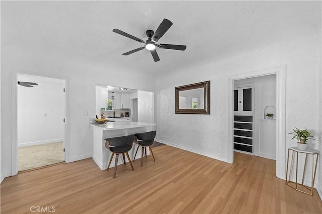 interior space with light wood finished floors, a kitchen bar, white cabinetry, and light countertops