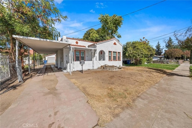 view of front of home with concrete driveway, stucco siding, an attached carport, fence, and a front yard