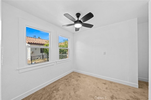 carpeted empty room with a ceiling fan and baseboards