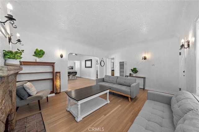 living area with arched walkways, a textured ceiling, and light wood-style floors